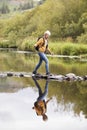 Senior Couple Crossing River Whilst Hiking In UK Lake District