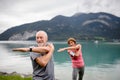 Senior couple doing outdoor yoga, tai chi, pilates by the lake in the autumn. Elderly husband and wife spending active Royalty Free Stock Photo