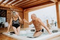 Senior couple enterying in outdoor bathtub at their terrace, during cold winter day.