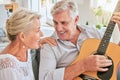Senior couple with guitar for music and singing together on sofa for retirement lifestyle and summer lens flare. Happy Royalty Free Stock Photo