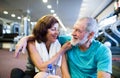 Senior couple in gym sitting in front of treadmills, resting