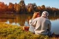 Senior couple having picnic by autumn lake. Happy man and woman enjoying nature and hugging Royalty Free Stock Photo