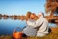 Senior couple having picnic by autumn lake. Happy man and woman enjoying nature and hugging Royalty Free Stock Photo