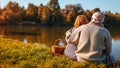 Senior couple having picnic by autumn lake. Happy man and woman enjoying nature and hugging Royalty Free Stock Photo