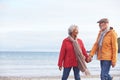 Senior Couple Hold Hands As They Walk Along Shoreline On Winter Beach Vacation Royalty Free Stock Photo