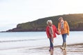 Senior Couple Hold Hands As They Walk Along Shoreline On Winter Beach Vacation Royalty Free Stock Photo