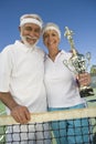 Senior Couple Holding Trophy At Tennis Net