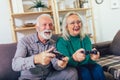 Senior couple at home playing video game holding joysticks in hands