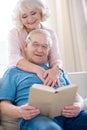 Senior couple hugging and relaxing, man reading book Royalty Free Stock Photo