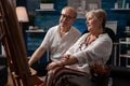 Senior couple looking at drawing sitting down in front of easel admiring creation Royalty Free Stock Photo