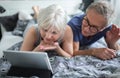 Senior couple lying on bed having video conversation