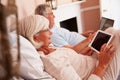Senior Couple Lying In Bed Using Digital Devices Royalty Free Stock Photo