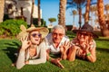 Senior couple lying on grass with adult daughter by hotel. Happy people enjoying vacation. Family values Royalty Free Stock Photo