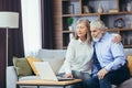 Senior couple man and woman sitting on sofa at home, gray-haired people using laptop, looking together at monitor screen Royalty Free Stock Photo