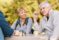 Senior couple playing chess in nature after a wellness, fresh air and health walk in a garden. Happy, smile and elderly Royalty Free Stock Photo