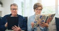 Senior couple, reading book and tablet on sofa in home, relax and internet search on social media. Elderly man, woman Royalty Free Stock Photo