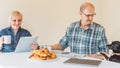 Senior couple reading news on digital tablet and old style newspaper while having breakfast in the morning Royalty Free Stock Photo