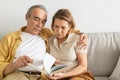 Senior couple reading story together, relaxing with book in the living room on sofa, free space Royalty Free Stock Photo