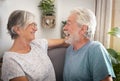 A senior couple relax on the armchair and laugh looking each other. Man with beard and white hair. Bright light from the window