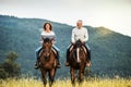 A senior couple riding horses in nature.