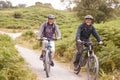 Senior couple riding mountain bikes in a country lane during a camping holiday smiling, front view