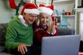 Senior couple in santa hat sitting on couch smiling while having a video call on laptop at home Royalty Free Stock Photo