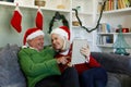 Senior couple in santa hat sitting on couch smiling looking at each other while using digital tablet Royalty Free Stock Photo