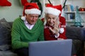 Senior couple in santa hat sitting on couch waving while having a video call on laptop at home Royalty Free Stock Photo