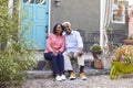 Senior couple sit on steps outside their house, full length