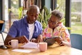 Senior Couple Sitting Around Table At Home Reviewing Finances Using Digital Tablet