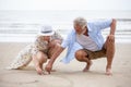 senior couple sitting on the beach drawing a heart in the sand together ,  woman asian man caucasian Royalty Free Stock Photo