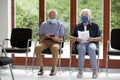 Senior couple sitting with face masks in a bright waiting room of a hospital or an office