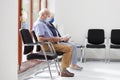 Senior couple sitting with face masks in a bright waiting room of a hospital or an office