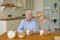 Senior couple sitting in the kitchen looking at the camera and drinking tea or coffee with cookies. Royalty Free Stock Photo