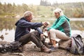 Senior couple sitting by a lake pouring coffee from a flask during a camping holiday, Lake District, UK