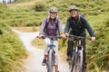 Senior couple sitting on mountain bikes in a country lane during a camping holiday, looking at camera, front view