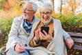 Senior couple sitting in public park using smart device to shop online