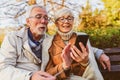 Senior couple sitting in public park using smart device to shop online