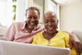 Senior Couple Sitting On Sofa Using Laptop At Home Together