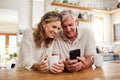 Senior couple on smartphone reading online social media post, search holiday house website or retirement planning