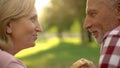 Senior couple smiling and enjoying picnic in park, male holding fast food burger Royalty Free Stock Photo