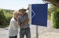 Senior couple with a sold sign outside their house