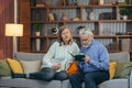 Senior couple spending leisure time reading a book together sitting on cozy sofa at home. Elderly mature family Gray hair man and