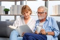 Senior couple spending time together in the living room, woman and man reading a book and enjoying coffee on the cozy sofa at home Royalty Free Stock Photo