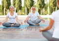 Senior couple staying in lotus pose in front of female yoga trainer during yoga class in city park Royalty Free Stock Photo