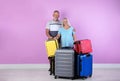 Senior couple with suitcases near color wall.