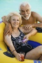 Senior Couple in Swimming Pool woman lying on inflatable raft holding drink listening to portable music player portrait. Royalty Free Stock Photo