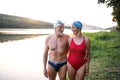 Senior couple in swimsuit standing by lake outdoors before swimming.