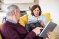 Senior couple with tablet and headphones sitting on sofa indoors at home. Royalty Free Stock Photo