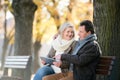 Senior couple with tablet sitting on bench. Autumn park. Royalty Free Stock Photo